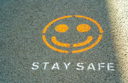 A yellow smiley face with the words ‘stay safe’ written under it on a road
