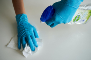 two gloved hands wiping a white surface with a cleaner and a paper towel