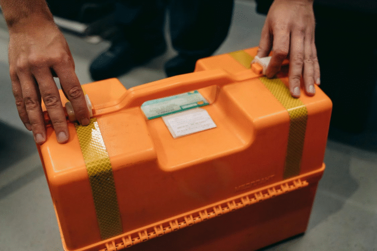 A person holding an orange hard plastic case with yellow reflective stripes and labels attached on top.