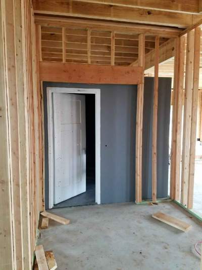 A white door installed in a gray safe room surrounded by unfinished wooden framing inside a building under construction.