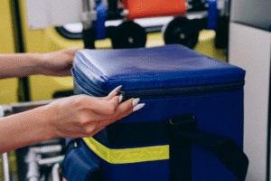 A person is unzipping a blue insulated emergency bag with a reflective yellow strip.