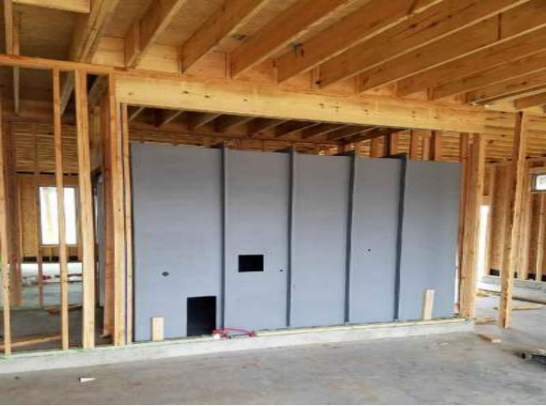 A large gray structure resembling a giant electrical outlet faceplate is humorously installed within the wooden frame of a house under construction.