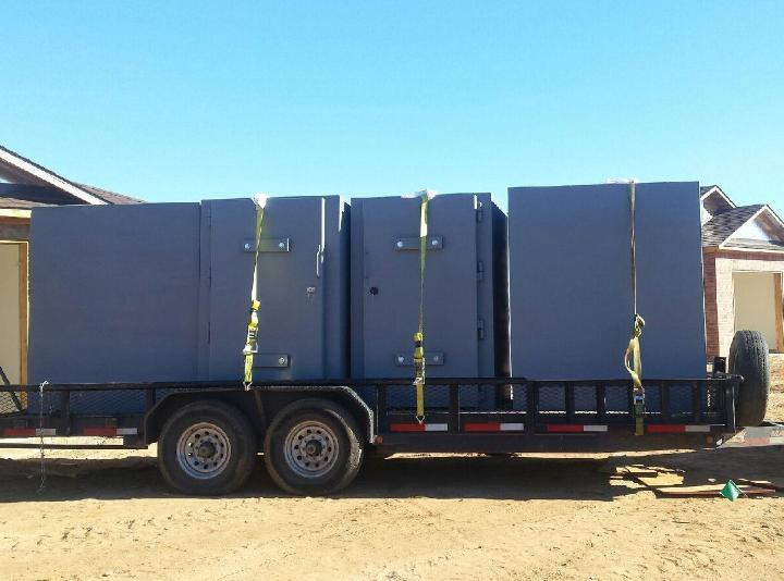 The image shows a trailer carrying multiple large, secured grey safes, tightly strapped for transport.