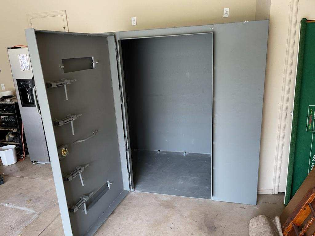 The image shows a large, open safe with a solid metal door, visible bolts, and an empty interior.