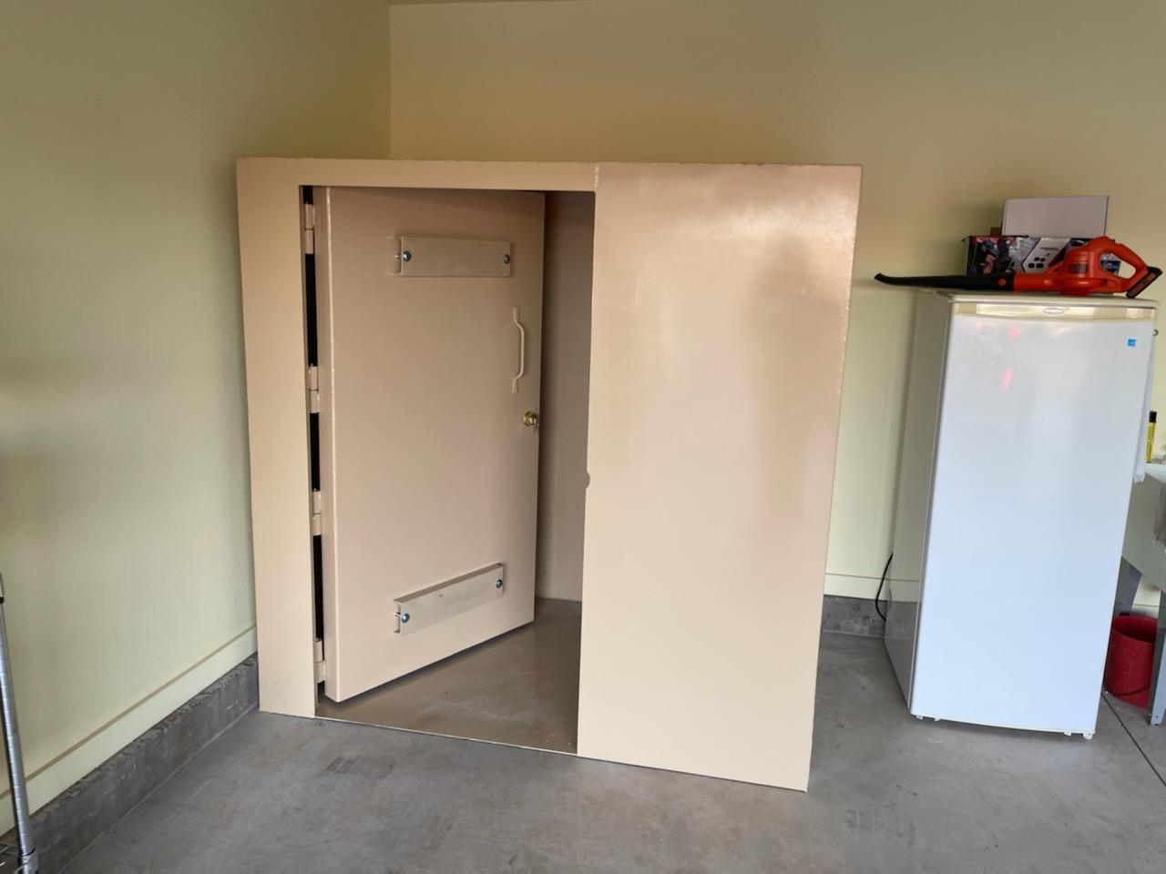 The image shows a beige vault or heavy-duty safe installed in a room, with a white fridge and other items nearby.
