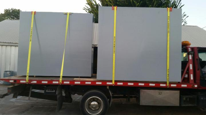 Two large gray structures resembling oversized electrical outlet faceplates are strapped onto a flatbed truck for transport.