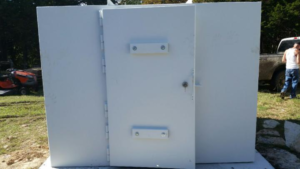 Storm shelter featuring a reinforced steel door installed on a concrete slab.