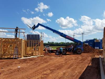 Construction equipment lifting safe room structure into place at a residential build site.