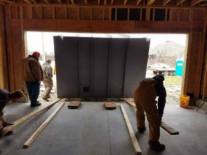 Workers positioning a reinforced safe room inside a residential garage during installation.