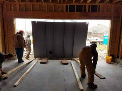 Workers positioning a reinforced safe room inside a residential garage during installation.