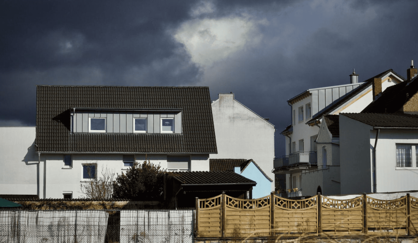 Above-ground safe room built beside a Texas home beneath dark storm clouds, illustrating fast access to shelter during severe weather.