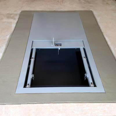 An underground shelter's flush floor hatch, shown open, installed into a carpeted floor.